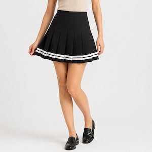 May include: A black pleated mini skirt featuring a high waistband and two horizontal white stripes near the hemline. The skirt has a structured, flared silhouette with sharp, evenly spaced vertical pleats that extend from the waist to the hem.