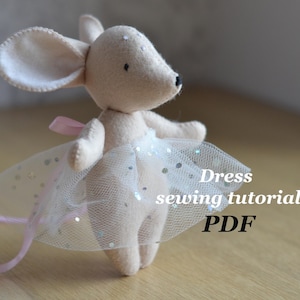 Könnte beinhalten: Ein Stoffmaus-Spielzeug mit einem weißen Tüll-Tutu mit silbernen Glitzerakzenten und einem rosa Band. Die Maus hat große Ohren und einen langen Schwanz. Der Text auf dem Bild lautet "Dress sewing tutorial PDF".