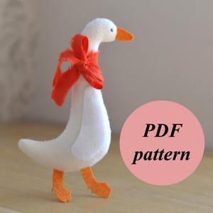 May include: A handmade white goose plush toy with orange feet and beak, and a red ribbon around its neck. The image includes the text "PDF pattern" in a pink circle, suggesting a craft project.