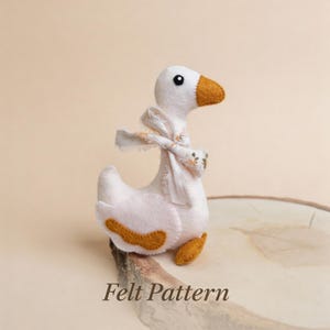 May include: A handmade white felt goose with a brown beak, feet, and wing accents. The goose has a patterned scarf tied around its neck. The text "Felt Pattern" is at the bottom of the image.