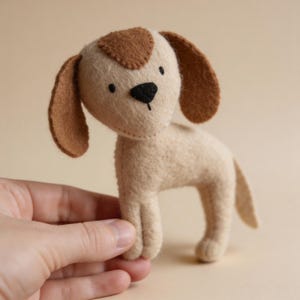 May include: A beige felt dog toy with brown details, including a head patch and ears. The toy dog has a black nose and is standing. The design is simple and charming, suitable for children. The toy is made of felt.