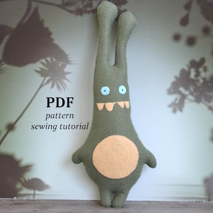 Può includere: Un peluche di mostro verde fatto a mano con una pancia arancione chiaro, occhi blu e un sorriso con i denti. Il peluche ha lunghe orecchie dritte e braccia e gambe piccole. Il testo sull'immagine recita "PDF pattern sewing tutorial".