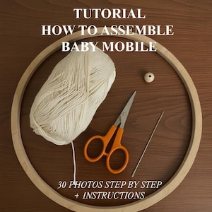 Könnte beinhalten: Ein hölzerner Stickrahmen mit einem Knäuel cremefarbener Wolle, einer orangefarbenen Schere, einer Nadel und einer Holzperle. Der Text lautet: "TUTORIAL HOW TO ASSEMBLE BABY MOBILE" und "30 PHOTOS STEP BY STEP + INSTRUCTIONS."