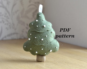 May include: A handmade felt Christmas tree ornament in olive green with white dot embellishments. The tree has a twine trunk and a white ribbon for hanging. The text "PDF pattern" is visible.