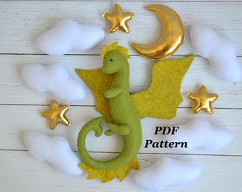 May include: A felt dragon with yellow wings and details, surrounded by white clouds, gold stars, and a gold crescent moon. The text "PDF Pattern" is visible. This is a craft project.