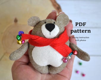 May include: A handmade felt bear with a red scarf and colorful bells. The bear has a white belly, a black nose, and gray ears. The text "PDF pattern" is visible, indicating a sewing pattern.