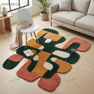 May include: An abstract area rug with a unique, organic shape. The rug features a combination of colors, including green, orange, yellow, and white. The design is modern and geometric, with various shapes and patterns. The rug is placed on a wooden floor.