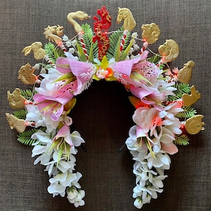 May include: A white floral headband with gold animal figurines and the word "Formosa" in red letters. The headband is decorated with white flowers and pink flowers.