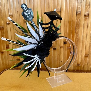 May include: Black and white Halloween headband featuring a spider web, black flowers, feathers, and a skeleton figure with the text "Dead Man".