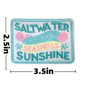May include: Embroidered patch with the words "SALTWATER, SEASHELLS, SUNSHINE" in turquoise, pink, and yellow. The rectangular patch is 3.5 inches wide and 2.5 inches tall. Features a beach theme with seashells and waves.
