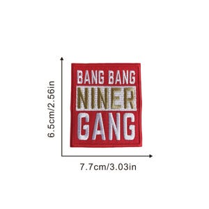 May include: A red embroidered patch with the words "BANG BANG NINER GANG" in white and gold lettering. The patch measures 3.03 inches wide and 2.56 inches tall. The patch is a rectangular shape.