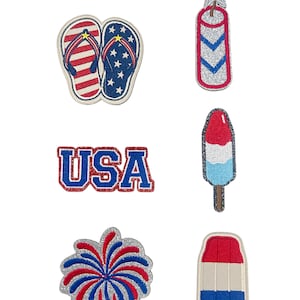 May include: A collection of patriotic-themed embroidered patches. Designs include red, white, and blue flip-flops, a firework burst, a popsicle, and the word "USA". Other patches feature a star and a red, white, and blue design.