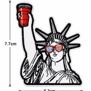 May include: Embroidered patch featuring the Statue of Liberty wearing sunglasses with an American flag design. She holds a red cup in her raised hand. The patch measures 7.7 cm high and 6.3 cm wide.