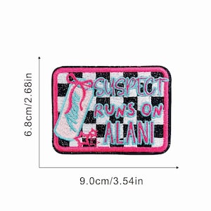 May include: Embroidered patch with a black and white checkered background and a pink border. The patch features the text "SUSPECT RUNS ON ALANI" in turquoise and pink, along with a turquoise shoe design. The patch measures 3.54 inches by 2.68 inches.