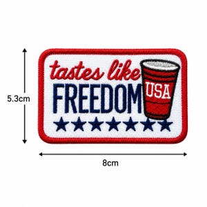 May include: Embroidered patch, 8cm wide and 5.3cm tall, with a red border and white background. The text "tastes like FREEDOM" is in red and blue. A red cup with "USA" is on the right, and there are six blue stars.