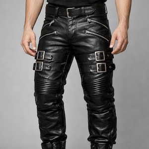 Puede incluir: Pantalones de cuero negro con cremalleras y hebillas plateadas. Los pantalones tienen un diseño ajustado con detalles acanalados en las rodillas y correas ajustables con hebillas plateadas. Un cinturón negro con hebilla plateada.
