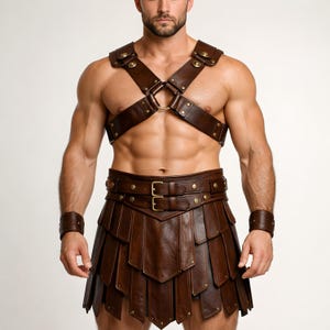 May include: Brown leather harness and skirt set. The harness has shoulder and chest straps joined by a metal ring. The skirt features layered panels and a double-buckle belt. Includes matching wrist cuffs. A unique costume.