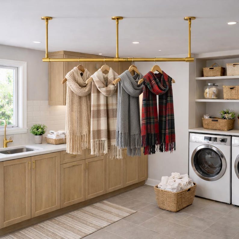 Pu&ograve; includere: Un appendiabiti in metallo dorato montato a soffitto che sostiene quattro sciarpe su grucce di legno. Le sciarpe includono un modello color crema a trecce, uno a quadri beige, uno in maglia grigia tinta unita e uno a quadri rossi, verdi e neri.