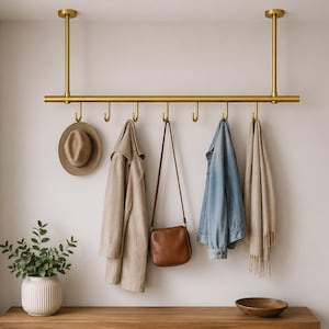 May include: A ceiling-mounted brass coat rack featuring a horizontal bar with eight evenly spaced hooks. The rack is suspended by two vertical rods attached to the ceiling, providing a storage solution for hanging items like hats, coats, and bags.