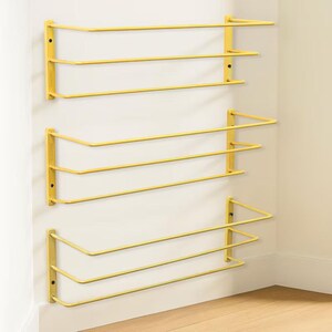 May include: Three yellow wall-mounted shelves, each featuring a rectangular frame with two horizontal bars extending outwards. The shelves are constructed from thin metal rods and are attached to the wall with vertical side brackets on each end.