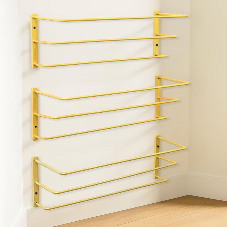 May include: Three yellow wall-mounted shelves, each featuring a rectangular frame with two horizontal bars extending outwards. The shelves are constructed from thin metal rods and are attached to the wall with vertical side brackets on each end.