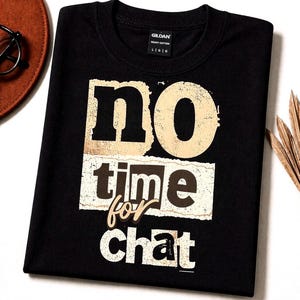 Può includere: T-shirt nero girocollo con la scritta "no time for chat" in un font vintage invecchiato. Il testo è beige e marrone, con un aspetto strutturato e invecchiato. La maglietta è realizzata in cotone pesante.