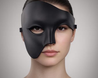 May include: A black half-face mask, covering the left eye and cheek, with a sleek, curved design. The mask is held in place with a thin strap. The mask is worn by a person with fair skin and dark hair.