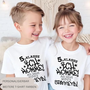 Op de afbeelding: Twee witte t-shirts met korte mouwen en zwarte grafische tekst met de tekst 5. KLASSE ICH KOMME! Ab jetzt wird's SPANNEND! De shirts hebben een ronde hals en zijn gemaakt van effen witte stof met dikke, donkere letters op de voorzijde.