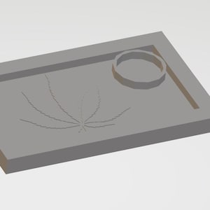 以下が含まれることがあります： 丸いへこみと大麻の葉のデザインが施された灰色の長方形のトレイ。トレイには隆起した縁があり、右下隅には青いダウンロードアイコンがあります。