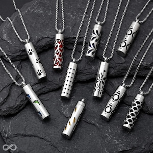 May include: A collection of nine silver-toned cylindrical pendant necklaces, each featuring unique cut-out patterns including paw prints, red hearts, dots, floral motifs, dolphins, and geometric shapes, all suspended on matching silver-toned chains.