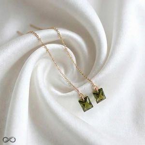 May include: A pair of gold-colored chain earrings with olive-green, rectangular gemstones. The earrings are displayed on a white, silky fabric. The gemstones are approximately 0.25 inches in length.