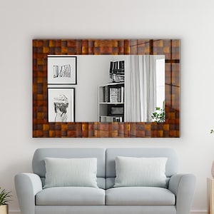 May include: A large rectangular mirror with a mosaic wooden frame in brown and copper tones. It hangs above a light blue sofa. The mirror reflects a room with a white curtain, shelves, and artwork. A light beige rug is on the wooden floor.