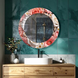 May include: A round wall mirror featuring a decorative border of printed pink, peach, and white roses and daisies. The reflective glass surface shows a partial view of a shower fixture, while the frame displays a dense floral arrangement.