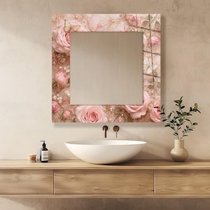 May include: A square wall mirror featuring a decorative border with a printed design of soft pink roses, white pearls, and delicate butterflies against a light pink background. The mirror has a reflective center and a smooth, flat glass surface.