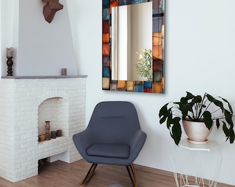 May include: Rectangular wall mirror with a colorful mosaic tile frame. The frame features a pattern of square tiles in shades of blue, orange, and brown. The mirror is hanging on a white wall above a gray chair.