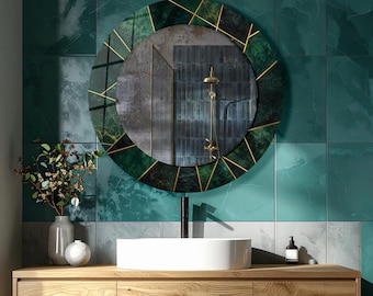 May include: A round wall mirror featuring a dark green marble-patterned frame with thin gold-colored geometric lines. The mirror reflects a shower head and tiled wall. It is positioned above a white vessel sink and a light wood vanity cabinet.