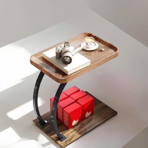 May include: A contemporary side table featuring a dark wood tray top, supported by curved black metal legs. A camera, book, and coffee cup are on the tray. Several red boxes are on the lower shelf. The table is designed for small spaces.