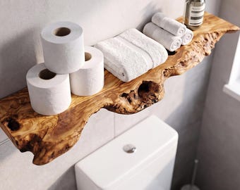 May include: A live edge wooden wall shelf featuring a natural grain pattern and irregular bark edges. The shelf holds two white toilet paper rolls, a folded white hand towel, two rolled white washcloths, and a clear pump bottle.