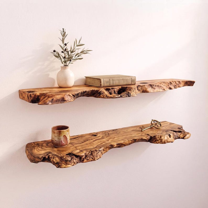 May include: Two wall-mounted shelves made from natural live-edge wood with a prominent grain pattern. The top shelf holds a small white vase with green sprigs and a rectangular book. The bottom shelf holds a small ceramic cup and a metal key.