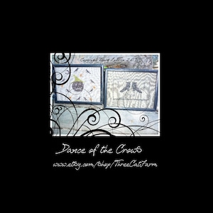 May include: Two framed cross-stitch patterns, one with a black jack-o-lantern and crows, the other with a pair of black boots. The text "Copyright Terry Leezen 2013" is visible in the top frame. The text "Dance of the Crows" and "www.etsy.com/shop/ThreeCatfarm" is below the frames.