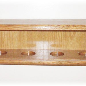 May include: A wooden wall-mounted shelf with five slots for storing pool cues. The shelf is made of light brown wood and has a curved front edge.