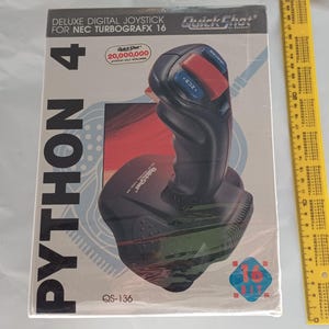 Könnte beinhalten: Ein QuickShot Python 4 Deluxe Digital-Joystick für NEC TurboGrafx 16 in der Originalverpackung. Die Schachtel zeigt den Produktnamen, eine 16-Bit-Grafik und ein gelbes Lineal, das eine Höhe von etwa 30 cm auf der rechten Seite anzeigt.