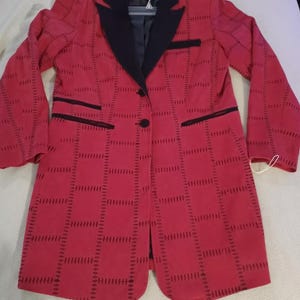 May include: A red blazer with a black collar and trim. The blazer has a unique stitched pattern design. It features a single-button closure and two front pockets. The blazer is hanging on a hanger.