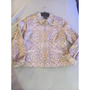 Puede incluir: Chaqueta rosa claro con un estampado de cachemira en tonos beige y lavanda. La chaqueta tiene cremallera completa, dos bolsillos delanteros y mangas largas. La chaqueta está colgada de una percha negra.