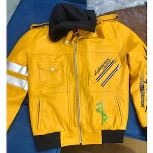 May include: Yellow leather jacket with a black hood and cuffs. Features silver stripes on the left sleeve, two diagonal zippers, and the text "Cyberpunk" and "Edge Runners" in black and green. Includes two front pockets.