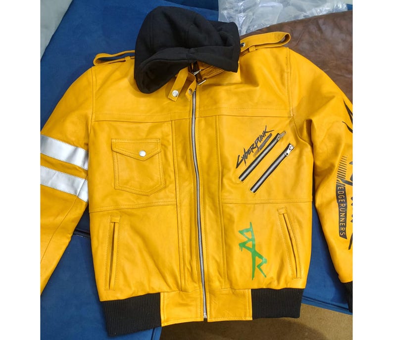 May include: Yellow leather jacket with a black hood and cuffs. Features silver stripes on the left sleeve, two diagonal zippers, and the text "Cyberpunk" and "Edge Runners" in black and green. Includes two front pockets.