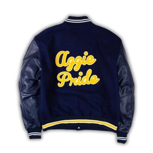 May include: Navy blue letterman jacket with leather sleeves. The back of the jacket features the words "Aggie Pride" in yellow script. The jacket has white and yellow striped trim on the collar, cuffs, and waist.