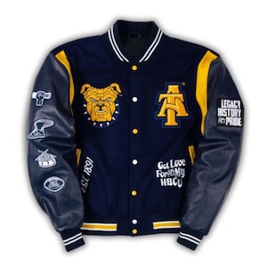 May include: Navy blue and gold varsity jacket with leather sleeves. Features a bulldog patch, the letters "A&T", and the text "Legacy History Pride" and "Got Love For My HBCU". The jacket has white and gold striped trim.
