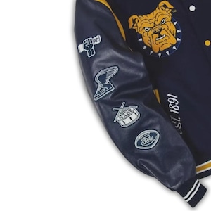 May include: Navy blue varsity jacket with yellow and white accents. Features a bulldog patch and various embroidered patches on the sleeve. The jacket has the text "EST. 1891" on the right side.