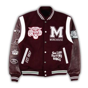 Può includere: Una giacca varsity marrone con maniche in pelle bianca, caratterizzata da una toppa con testa di tigre, una grande lettera M e il testo Morehouse, Est. 1867 e Got Love For My HBCU. Le maniche includono toppe a forma di pugno, scarpa, tamburo e football.